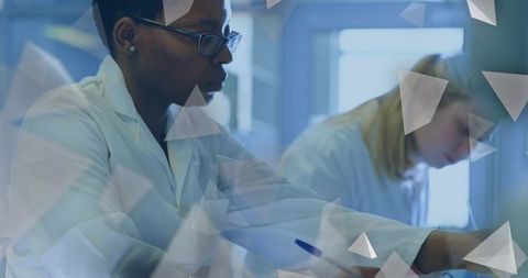 Female scientist writing notes in laboratory while colleague collaborating in background