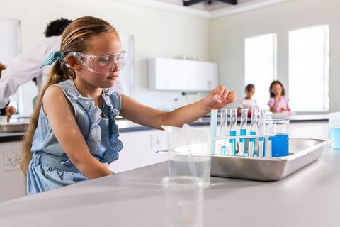 Young girl in safety goggles mixing colorful chemicals in test tubes