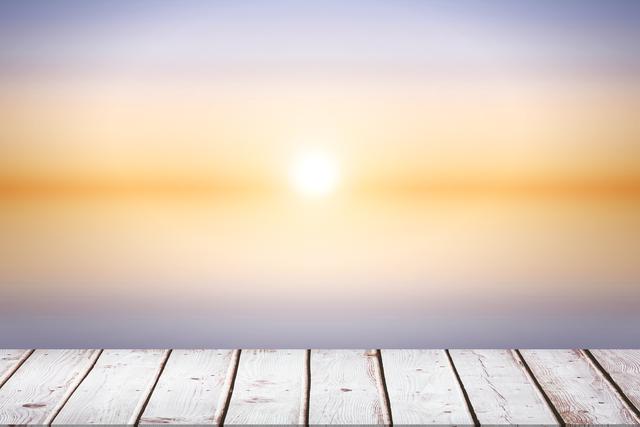 This image shows wooden boards in the foreground with a serene sunset in the background. The calm horizon and gradient sky create a tranquil atmosphere. Ideal for use in advertisements, website headers, backgrounds for inspirational quotes, or any project needing a peaceful and natural setting.