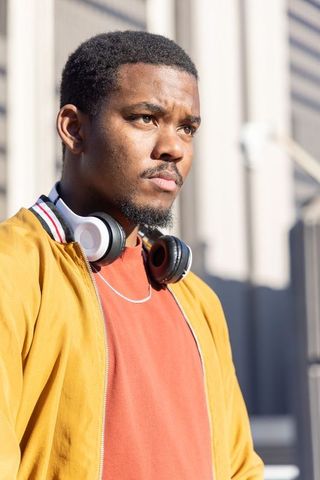 Contemplative african american man wearing headphones standing in sunlit city portrait