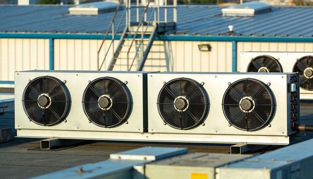 Rooftop hvac condenser unit with four fans and piping casting shadows during golden hour
