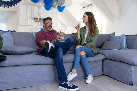 Mature couple enjoying wine on gray sectional sofa during blue birthday celebration