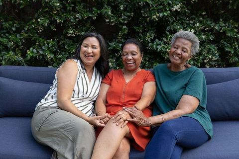 Laughing african american women sitting together on outdoor sofa holding hands