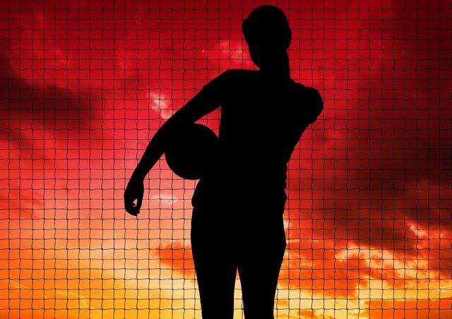 Silhouette of player holding a ball against net and orange sky in background