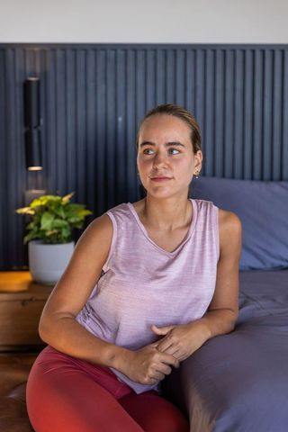 Young woman relaxing on modern bedroom bed wearing mauve top and red leggings