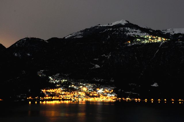 Mountain village at night with a serene atmosphere, lights from the homes and streets creating a warm contrast. Perfect for backgrounds, travel advertisements, winter holiday promotions, and articles about rural lifestyles.
