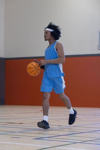 Male basketball player dribbling across indoor gym court