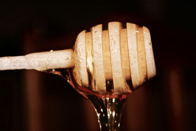 Close-up shot of a wooden honey dipper with honey dripping off it. Perfect for use in advertisements for honey products, kitchen gadgets, or natural ingredients. Ideal for food blogs, recipe sites, or educational materials about beekeeping and honey production.