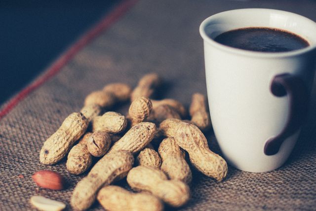 Scene shows a rustic setting with whole peanuts spilling over burlap cloth and a coffee mug beside them. This can be used for food blogs, kitchen decor, nutrition articles, or promoting coffee and snack pairing.