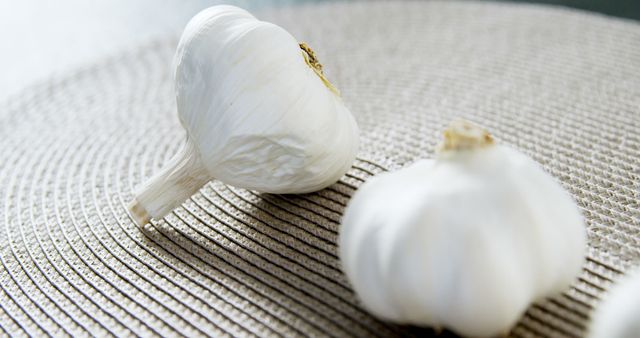 Fresh garlic bulbs resting on woven place mat, emphasizing texture and natural look. Ideal for food blogs, recipes, menu designs, health articles, and culinary websites.