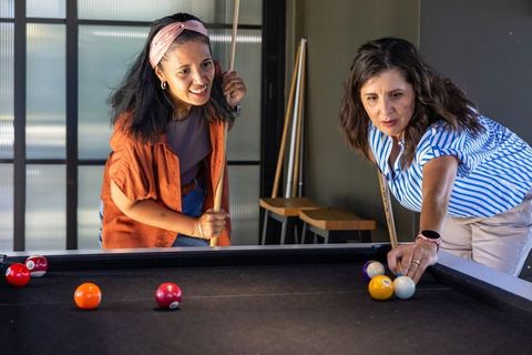 Diverse women playing pool in modern lounge showing friendship, fun, casual recreation
