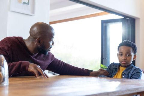 African american father comforting son at kitchen table during serious conversation