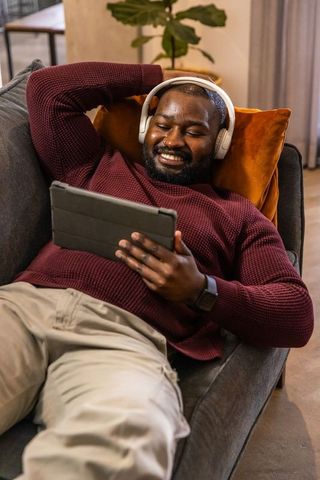 African american man relaxing on sofa with tablet and headphones in cozy home