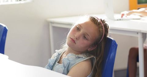 Schoolgirl leaning back in classroom chair looking pensive during daylight lesson