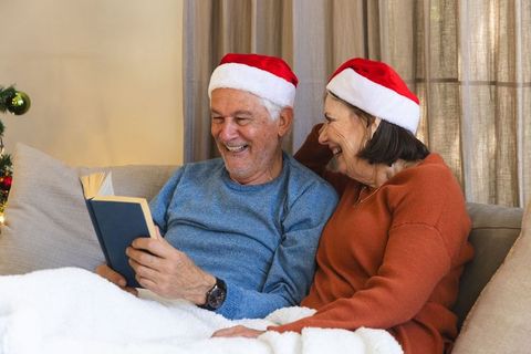 Senior Couple Relaxing with Christmas Book by the Fireplace