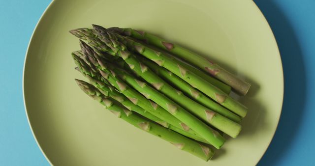 Image of fresh asparagus on green plate over blue background. fusion food, fresh vegetables and healthy eating concept.