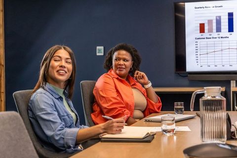 Diverse female coworkers discussing quarterly data and growth charts during boardroom meeting