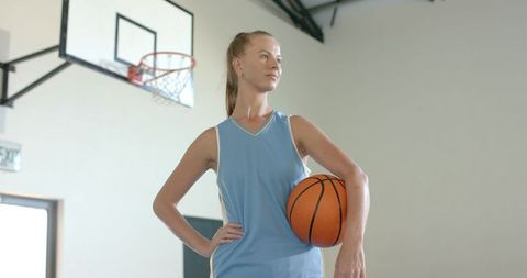 Confident Female Athlete Holding Basketball in Gym