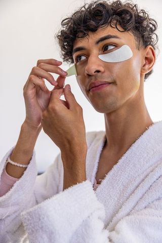 Young Man Applying Eye Patches for Skincare Routine in Bathroom