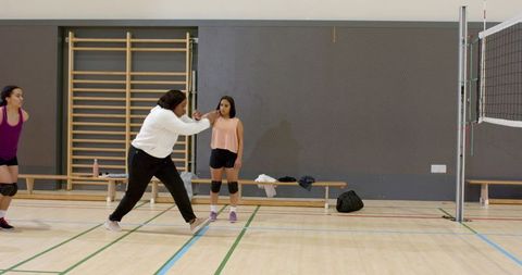 Diverse female volleyball coach demonstrating passing drill with young players in gym