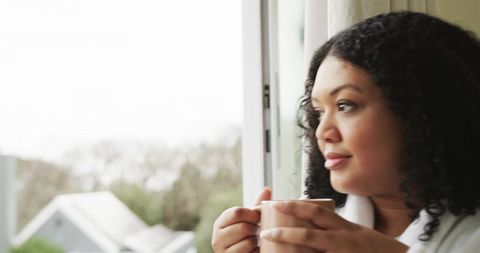 Morning calm woman gazing out window holding mug in cozy white robe soft natural light
