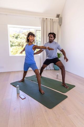 Young african american couple practicing warrior ii yoga at home on green mats