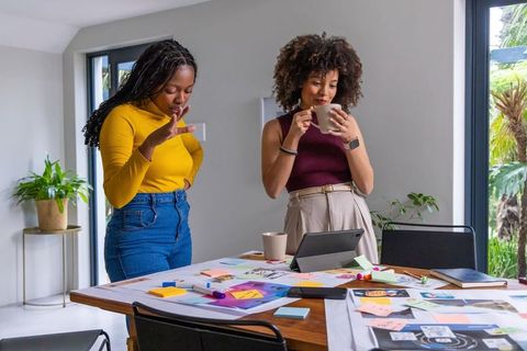 African american women collaborating, brainstorming around tablet with sticky notes
