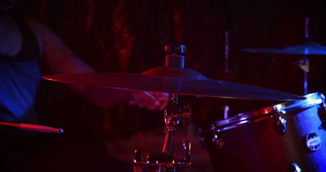 Drummer performing with drum set in dimly lit room. Focus on cymbals and drum equipment under dramatic stage lighting. Ideal for depicting music performances, live concerts, music practice scenes, or creating an intimate atmosphere for music-related projects. Perfect for promoting musical events, drum classes, or band promotions.
