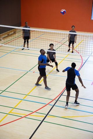 Multiracial men playing competitive indoor volleyball on hardwood gym court