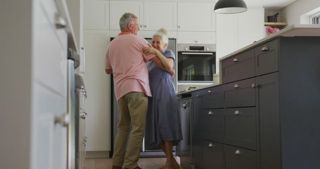 Elderly couple find joyously dancing in their modern, brightly lit kitchen, showcasing uninhibited love and companionship. Perfect for advertising retirement homes, senior lifestyle products, home care services, or brochures illustrating the beauty of aging together. Portrays themes of love, intimacy, and an active, happy retired life.