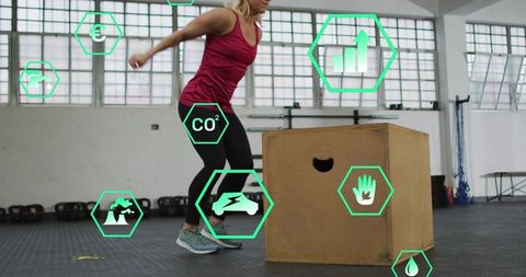 Mid-adult woman performing plyometric box jumps in gym with fitness and eco icons overlay