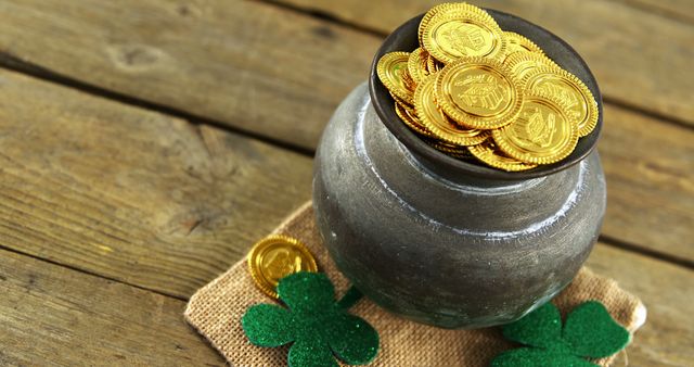 A pot filled with gold coins sits atop a rustic wooden surface, accompanied by green shamrocks, symbolizing wealth and luck often associated with St. Patrick's Day celebrations. The arrangement evokes festive Irish traditions and the lore of leprechauns hoarding pots of gold at the end of rainbows.