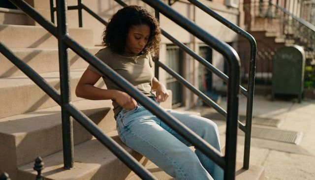 Woman adjusting jeans on brownstone stoop with sunlight, railings and urban calm