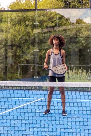 Woman playing padel on blue court holding racket with glass panels and green backdrop