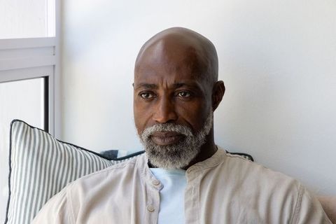 Senior man sitting on sofa gazing out window, contemplative home portrait for wellness