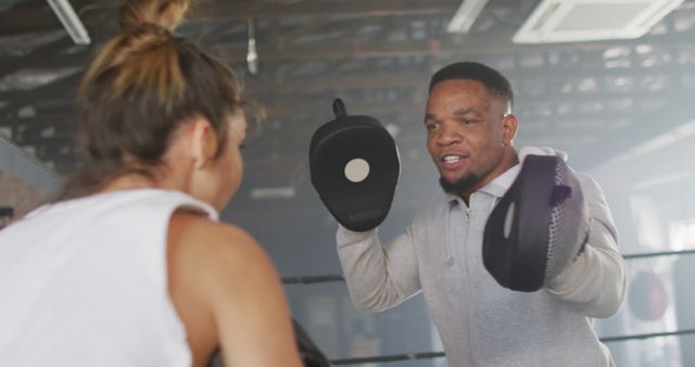 Personal trainer coaching a client in a boxing gym setting. Trainer holds punching mitts while giving instructions. Great for articles, fitness blogs, and promotional material for gym memberships or personal training services.