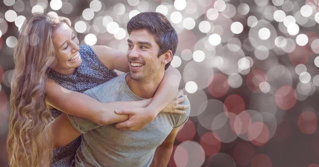 Man giving piggyback ride to woman while both are smiling against a glittery, bokeh background. Ideal for use in advertisements, social media, relationship blogs, or any context needing a visual representation of love, joy, and togetherness.