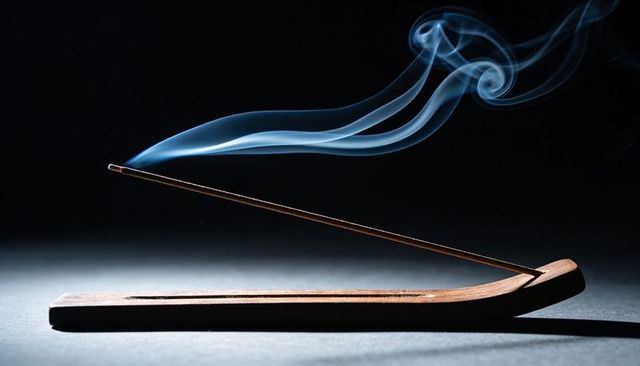 Smoldering incense stick emitting graceful blue-gray smoke above wooden boat holder