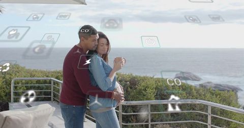 Expectant couple embracing on ocean balcony with virtual wellness and smart home icons