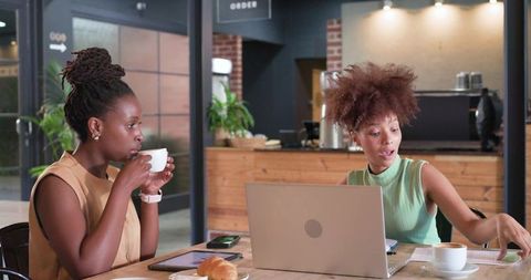 Cozy cafe coworking: two women collaborating over laptop and coffee during casual brainstorming