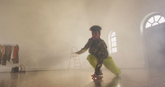 Capturing a contemporary dancer striking a dynamic pose in a modern studio filled with atmospheric smoke. The dancer is dressed in stylish, trendy clothing, adding to the vibrant energy of the moment. This setting might include elements like art and fashion. This image can be used in marketing and promotional materials for dance classes, performing arts events, or lifestyle brands targeting energetic and creative audiences.