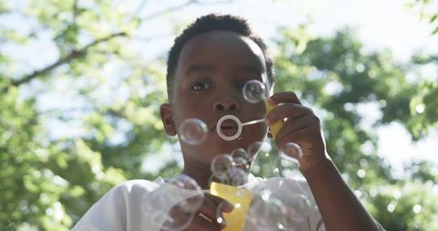 African american boy blowing bubbles in sunlit park capturing childhood joy