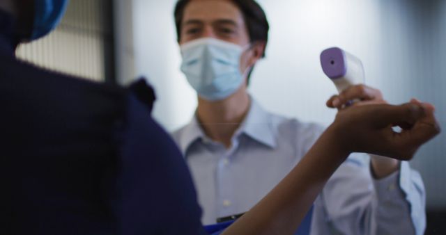 Caucasian businessman wearing face mask checking coworkers temperature. hygiene in business workplace social distancing during covid 19 coronavirus pandemic.