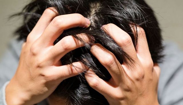Man gripping hair pressing scalp closeup expressing stress frustration anxiety and headache