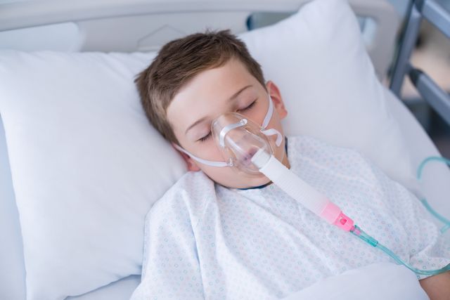 Close-up of boy patient wearing oxygen mask lying on hospital bed