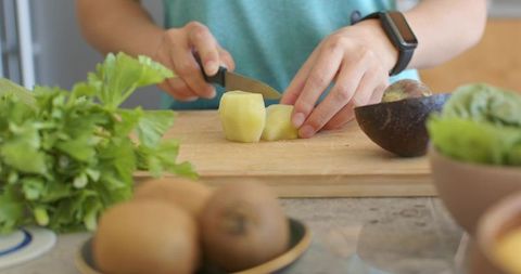 Asian woman slicing peeled potato on wooden cutting board with avocado and greens