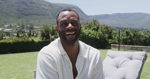Laughing african american man relaxing on lounge chair in sunny garden with mountain view