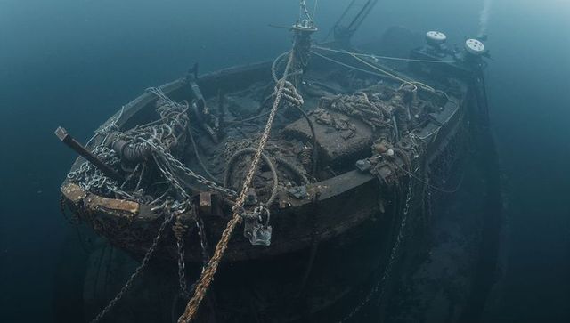 Sunken wooden boat bow with tangled ropes, chains and corroded winches barnacled on seabed