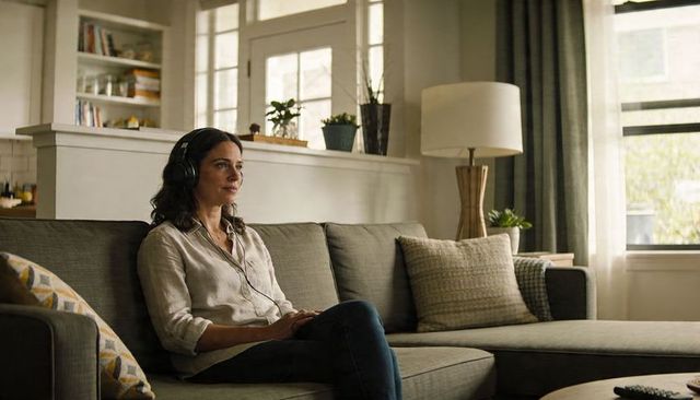 Woman listening to music with headphones relaxing on sunlit gray l-shaped sofa