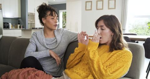 Friend comforting unwell companion on couch in modern living room, cozy knit sweaters